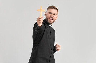 Wall Mural - Emotional young priest with cross on light background