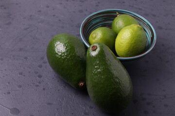 exotic tropical green citruses (limes) and avocados on the dark grey concrete stone surface. space for text. minimalism style. top view