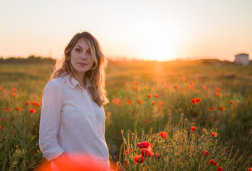 woman of European race standing in the  field with poppies on the sunset and enjoy nature. Copy space.