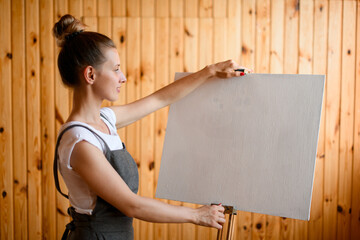 young woman artist stands in front of easel and holds the canvas with her hands