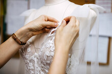 Close-up Of Work Process Of A Tailor In Her Studio. Hands Sewing Bridal Dress Process, Pinning Lace On Mannequin.
