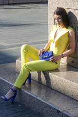 Wall Mural - Outdoor portrait of young fashionable woman wearing a yellow jumpsuit and blue accessories