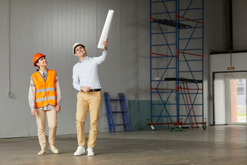 Wall Mural - Engineer in work helmet pointing at something and explaining the process of work to worker they standing in empty building