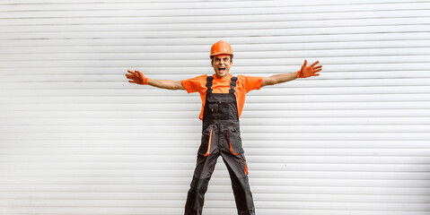 Wall Mural - Young happy laughing caucasian man builder construction worker in a safety helmet is shaking hands in front of the roller door lifting gates