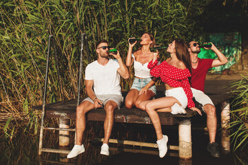 Wall Mural - Happy group of young people drinking beer on a dock by the river during the summer sunny day