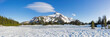 Wide panoramic view of a volcanic mountain peak under a crisp blue sky rising behind a field of snow.