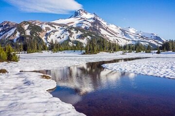 Wall Mural - volcanic mountain peak under a crisp blue sky rises behind a field of snow. calm water in the foregr