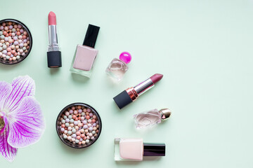 Decorative flat lay composition with lipstick and blush, decorated with flowers. Top view on soft green background.Stylish design background. Creative fashionable concept.Tools of women beauty