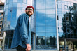 © mykolastock - Happy young trendy bearded hipster male dressed in casual denim shirt, red hat and eyeglasses looking away and smiling