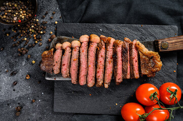 Grilled sliced marbled beef steak on a meat cleaver. Black background. Top view