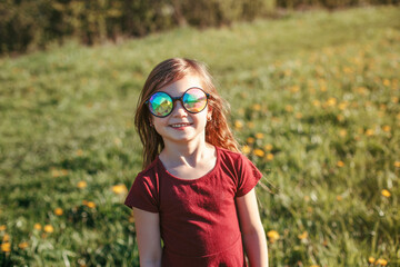 Happy smiling young Caucasian girl in funny sunglasses posing outdoors. Cute adorable kid child having fun outside. Happy childhood lifestyle. Sincere positive emotion.