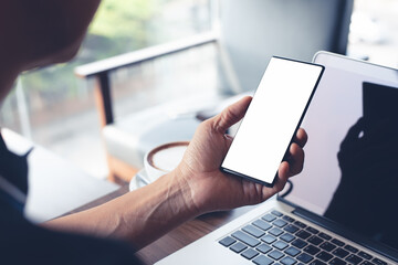 Canvas Print - Mockup of man hand holding and using mobile phone while online working on laptop computer in coffee shop