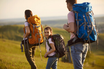 A happy family and a child with backpacks are lying on the grass in nature.