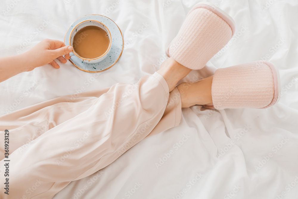 Woman in soft slippers drinking coffee in bedroom