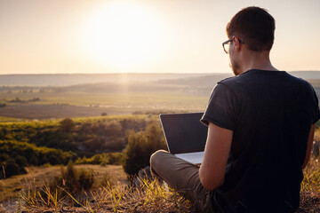 man with laptop sitting on the edge of a mountain with stunning views of the valley