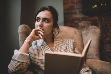 Contemplative female student thoughtful looking away during time for analyzing informative notes from knowledge notebook, pensive author pondering on article ideas sitting in comfortable armchair