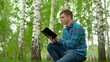 © Vital9c - A young man is sitting in nature with a book in his hands. A man sits on a stump in a birch forest and reads a book.
