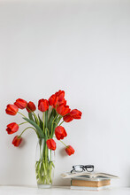 Red Tulips In A Vase, Books And School Supplies On A White Background. The Concept Of A Postcard For Teacher's Day. Copy Space.