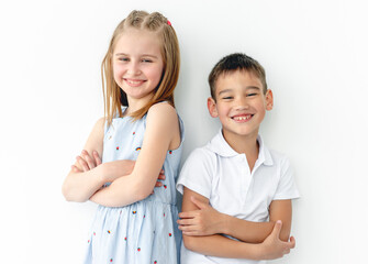 Happy children with crossed hands leaning against white wall