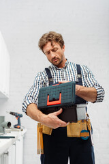 Wall Mural - Handsome plumber in overalls holding toolbox in kitchen