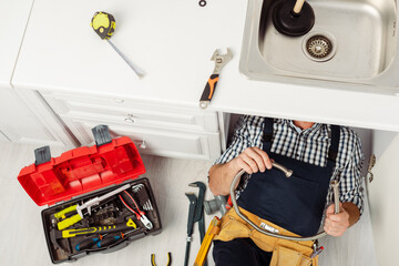 Wall Mural - Top view of plumber holding metal pipe while repairing kitchen sink near tools on worktop and floor