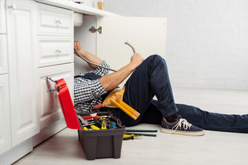 Canvas Print - Selective focus of plumber holding metal pipe while fixing kitchen sink near instrument and toolbox in kitchen