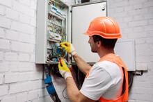 Handsome Electrician In Hardhat And Gloves Holding Multimeter Near Electrical Distribution Box