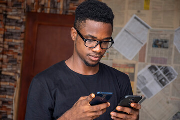 side view of a young african man using two mobile phones simultaneously