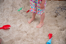 Drop Down View Of Sand Toys On Beach With Child Feet Standing Near.