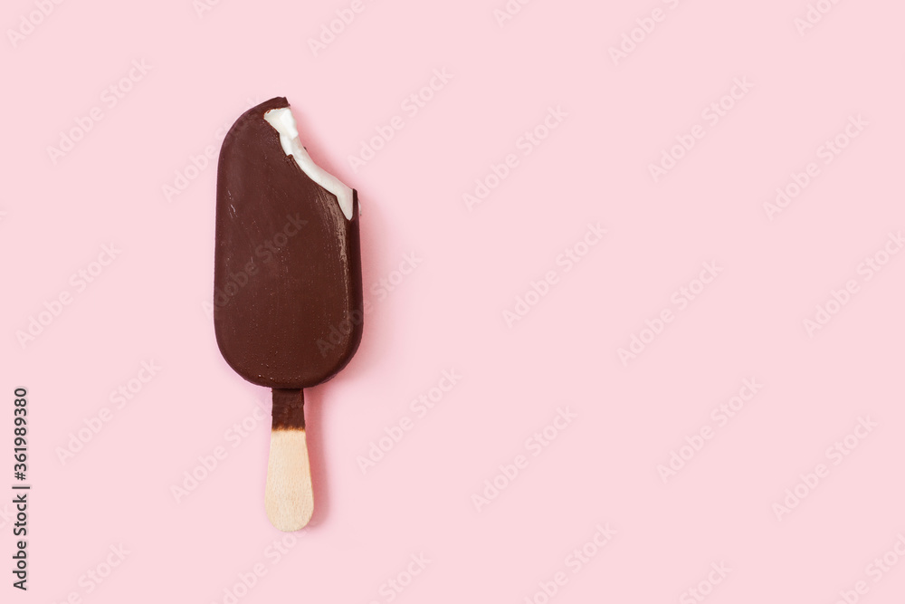 Helado de chocolate de palo batuta con una mordida sobre un fondo rosa pastel liso y aislado. Vista superior. Copy space - obrazy, fototapety, plakaty 