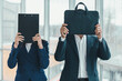 © Andrii - Woman hiding her face behind clipboard, man hiding his face behind laptop case.