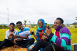 © Courage - young black people sitting in a park, drinking from their glass cups and using smartphone