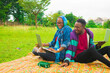 © Courage - young black couples sitting down in a park, using their laptops to surf the internet