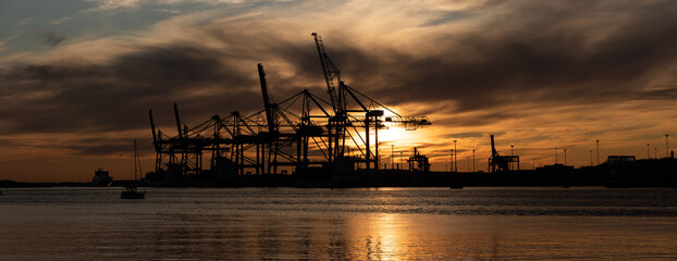 Wall Mural - Silhouettes of ship to shore cranes at sunset.