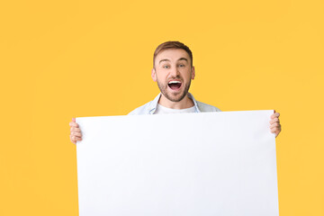 Wall Mural - Excited young man with blank placard on color background