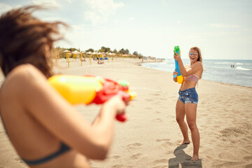 Wall Mural - two fit women playing with water-guns on sandy beach