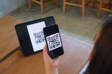 Women's hand uses a mobile phone application to scan QR codes in stores that accept digital payments without money and plastic tags on the table. QR code payment and cashless technology concept