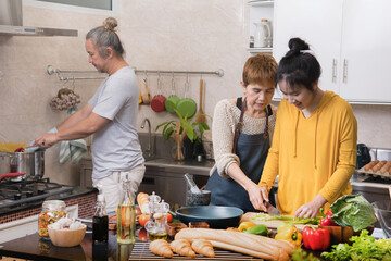 Wall Mural - Happy Asian family of mother father and daughter cooking in kitchen making healthy food together feeling fun