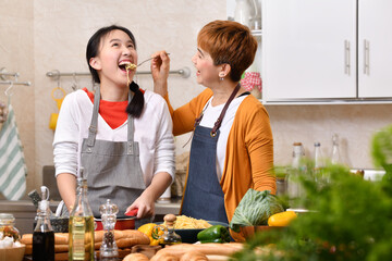 Wall Mural - Loving Asian family of mother and daughter cooking in kitchen making healthy food together feeling fun