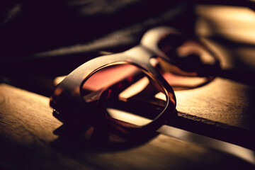 Selective focus close up shot of a pair of sunglasses on the wooden table of a bar. Natural lighting, sun rays, summer feeling, warm colors.