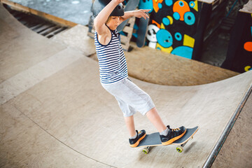 Wall Mural - Child skateboarder during learning tricks on a ramp in an urban skate park. boy in a sports helmet rides on a skate board at a sports venue. Active extreme kids spending time. guy skateboarder rides