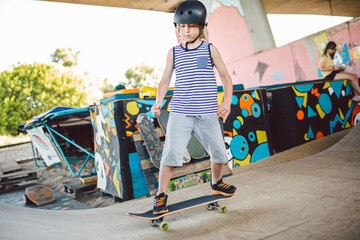 Wall Mural - Skater boy rides on skateboard at skate park ramp. Kid practising skateboarding outdoors on skatepark. Youth culture of leisure and sports. Skateboarder doing trick on skateboard on halfpipe ramp