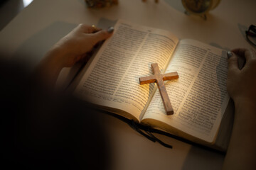 asian woman praying and holding a cross with her bible on table. online church from home concept.