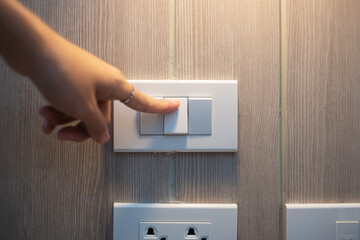 Female finger is turn on or off on light switch on white wall at home. Energy Saving, power, electrical and lifestyle concepts .