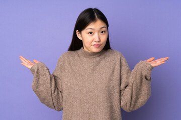 Wall Mural - Young asian woman isolated on purple background having doubts while raising hands