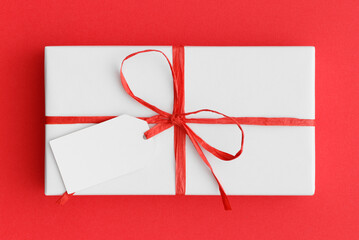 Sticker - White christmas gift with a blank tag mockup on a red background.