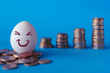 Faces on the eggs, investment concept. Happy investor smiling in front of his growing money. Blue background with stacks of coins