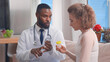 © TommyStockProject - Young african male doctor with bottle of pills in hands treating patient at home