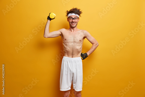 Cuadros en Lienzo Sporty man makes easy exercise on biceps, raises hand with dumbbell, leads healt