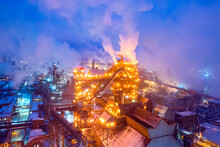Night Top View Of Steel Plant At Night With Smokestacks And Fire Blazing Out Of The Pipe. Industrial Panoramic Landmark With Blast Furnance Of Metallurgical Production